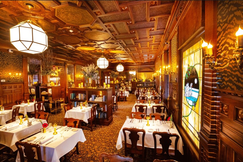 Ein gemütlich beleuchtetes Restaurant mit Holztischen und -stühlen, gedeckten Tischen und einer dekorativen Decke. 1