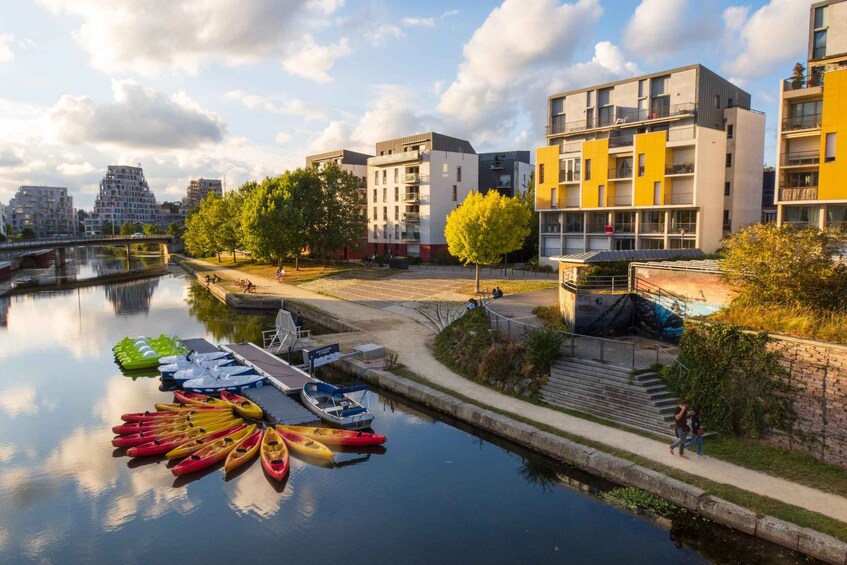 A canal with kayaks docked, modern buildings, and a bridge in the background. 2
