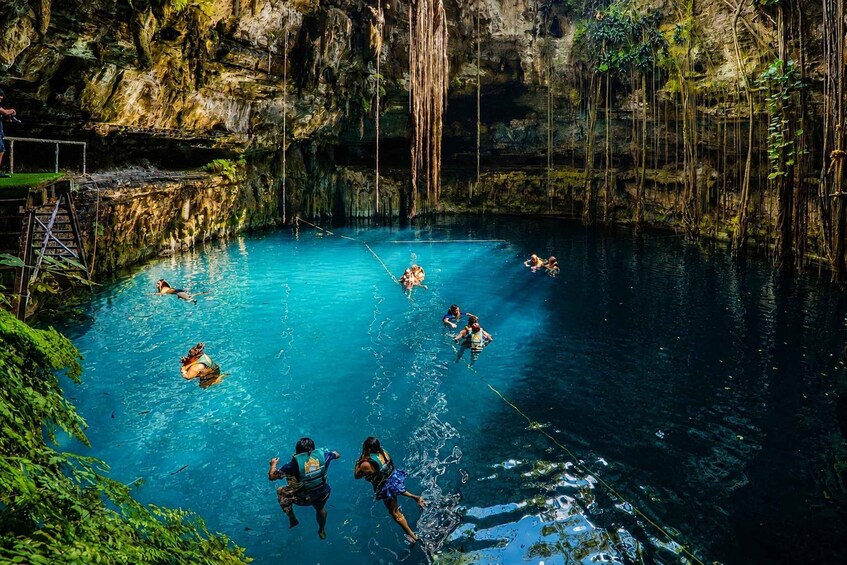 A group of people swimming in a clear blue pool surrounded by rocky cliffs and greenery. 1