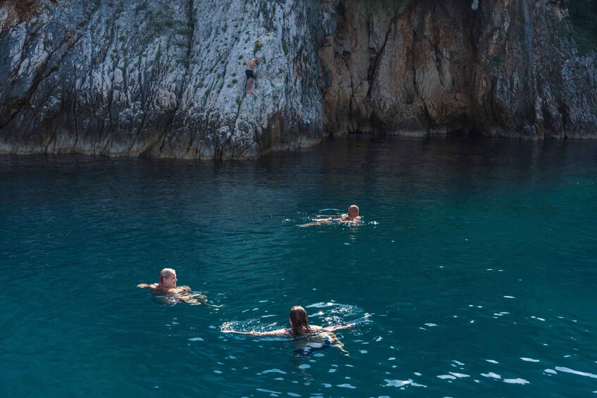 Trois personnes nagent dans une étendue d’eau claire et bleue, avec des falaises rocheuses en arrière-plan. 2