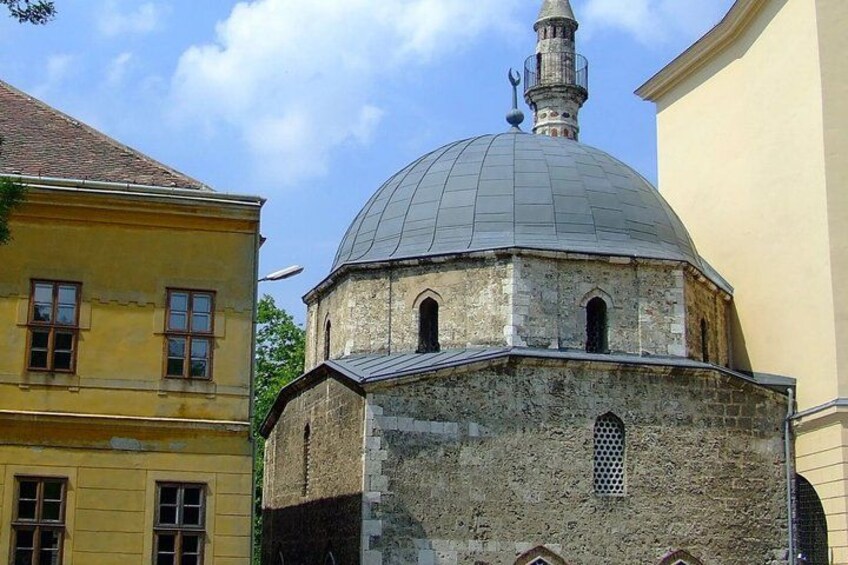 A historic building with a dome and a minaret, surrounded by other buildings. 1