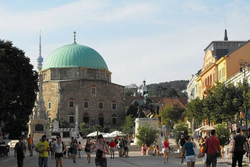 A historic building with a green dome, a statue, and a busy public square with people. 4