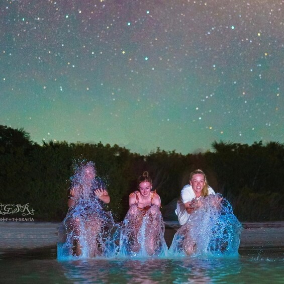 Three people in water with water spraying upwards, under a starry night sky. 2