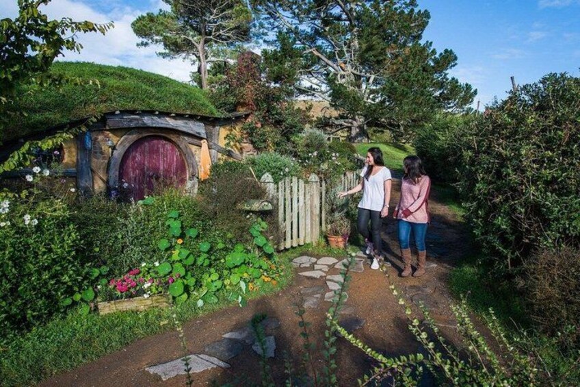 A Hobbiton-style house with a round door, a wooden fence, and lush greenery. 1