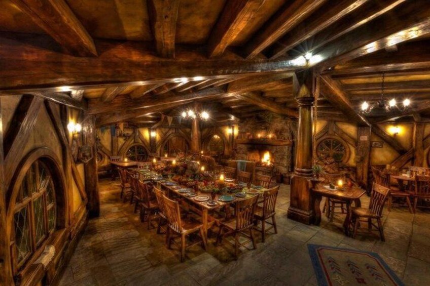A wooden dining hall with high ceilings, exposed beams, and a long table set for a meal. 2