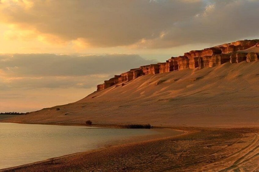 A desert landscape with a large body of water, a sandy beach, and a rocky cliff. 3
