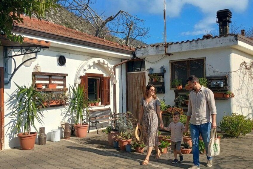 A family walking in a courtyard with a white house, potted plants, and a wooden bench. 4