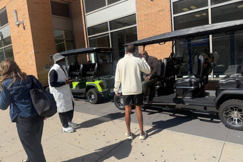 People standing on a sidewalk, a golf cart, and a building with a large window. 4