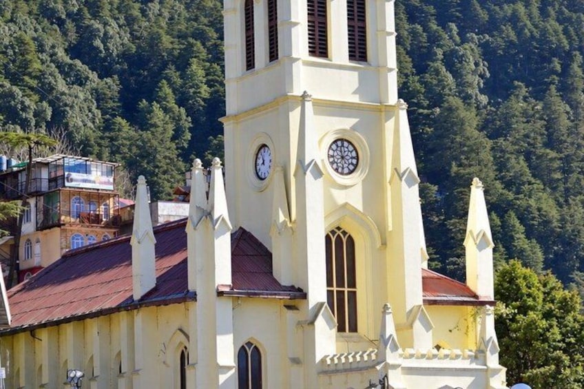 A church with a clock tower, surrounded by forested hills. 1