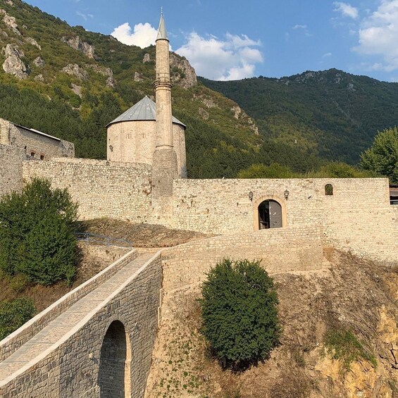 A stone fortress with a tower, surrounded by a stone wall and a bridge. 5
