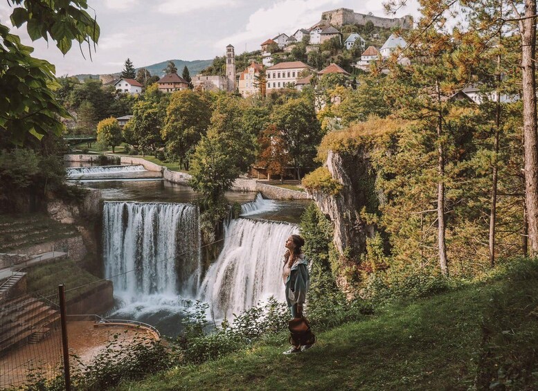 A waterfall, a person, and a town with buildings and a castle in the background. 1