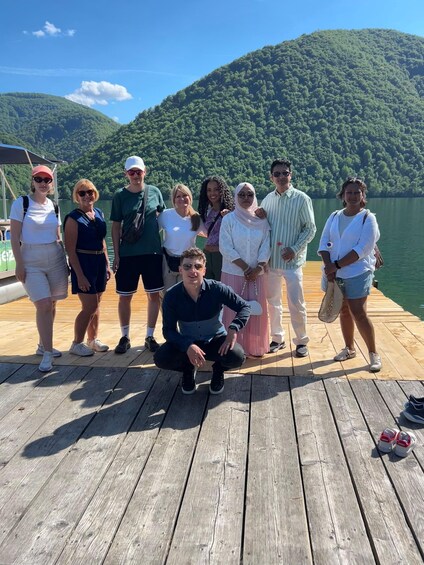 A group of people on a wooden dock by a lake with a forested hill in the background. 2