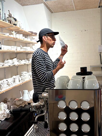 A person in a striped shirt and cap holding a white object, standing in a room with shelves of white ceramic items and a coffee machine. 4