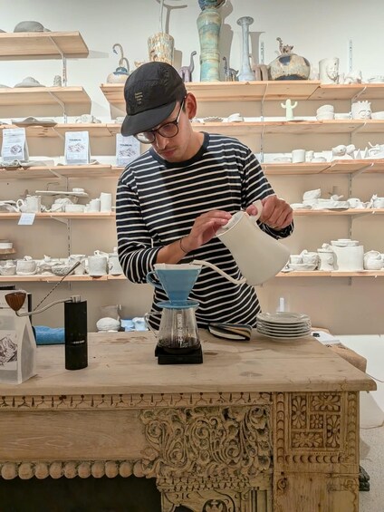 A person pouring coffee from a blue drip coffee maker into a white mug. 1