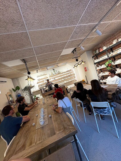 A group of people seated at a wooden table in a cafe with a ceiling made of straw-like material, shelves with pottery, and hanging plants. 5