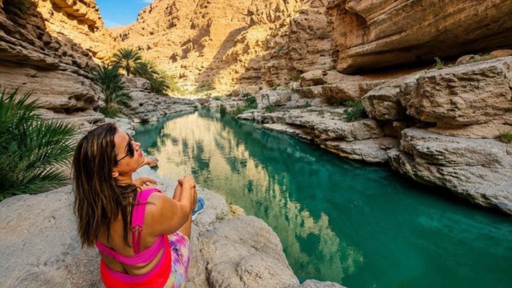 Una persona sentada sobre una roca junto a un río turquesa en un cañón. 3