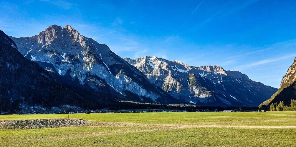 A mountain range with a clear sky, a green field in the foreground, and a village in the midground. 3