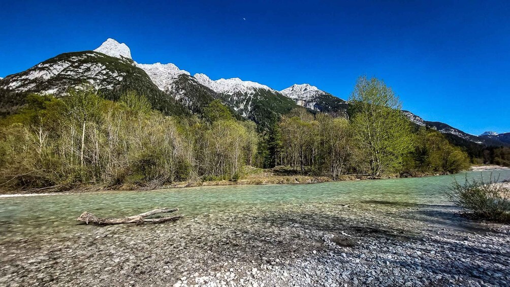 A clear river with rocky banks, surrounded by forested mountains under a blue sky. 5