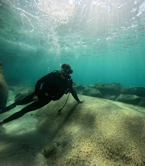 A diver underwater, surrounded by rocks and sandy ocean floor. 2