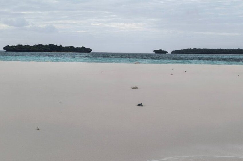A sandy beach with calm water and two small islands in the distance. 3