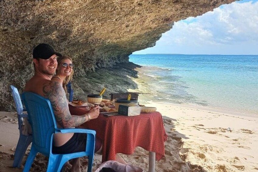 A couple dining under a rock overhang by the beach. 4
