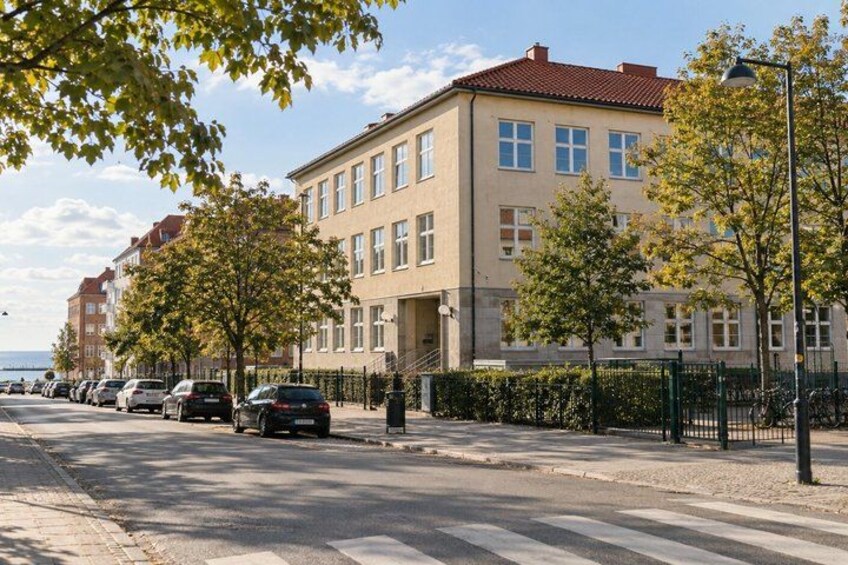 A street with parked cars, a row of trees, and a building with a red roof. 5