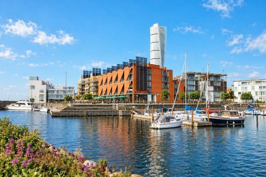 A marina with boats, a modern building with a unique tower, and a clear blue sky. 3