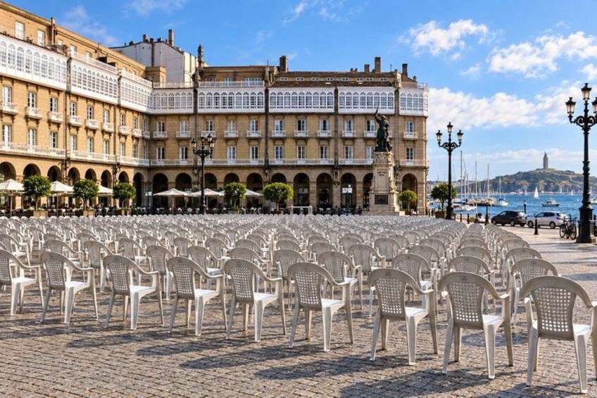 A plaza with rows of white plastic chairs, a historic building with balconies, and a statue in the background. 4