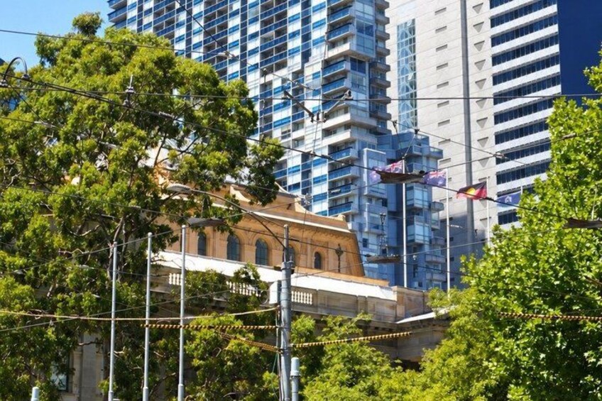 A historic building with a red facade, surrounded by modern high-rise buildings and lush green trees. 2