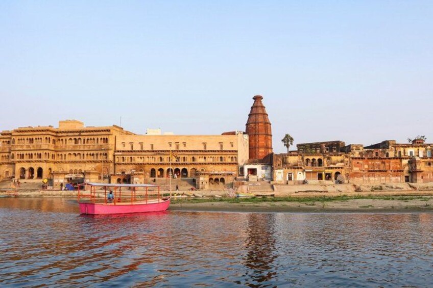 A river with a pink boat, historic buildings, and a tall tower by the water. 4