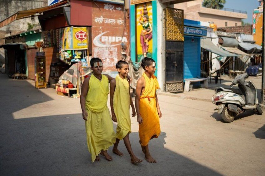 Two individuals in traditional attire walking on a street with shops and a scooter in the background. 5