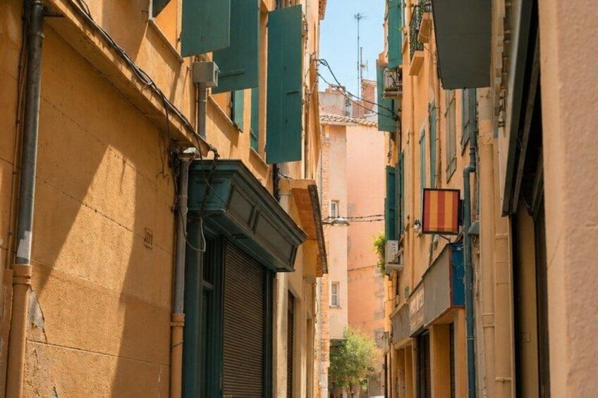 A narrow street with buildings, shutters, and a flag. 5