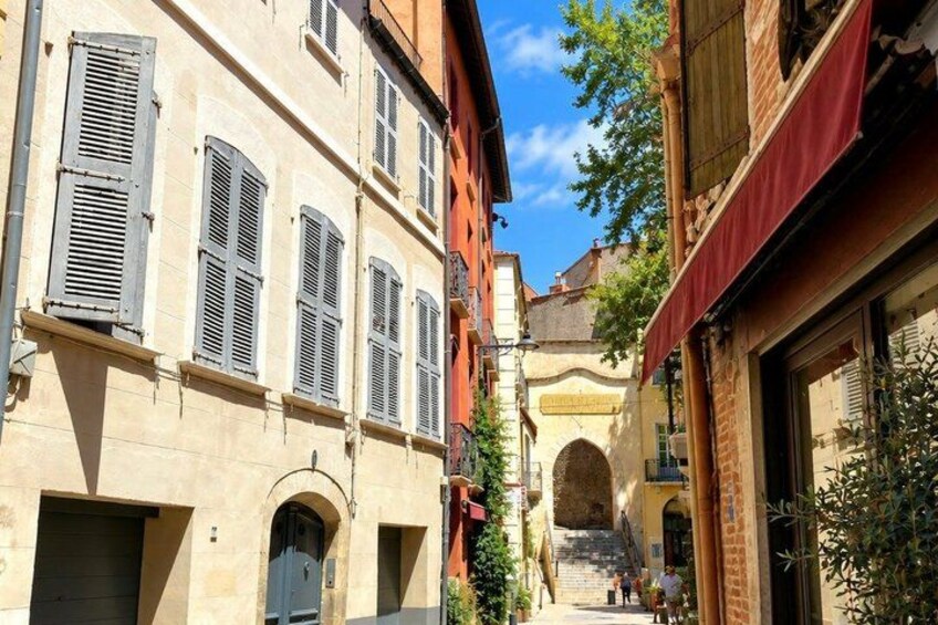 A narrow street with buildings, a blue door, and a staircase leading to an archway. 3