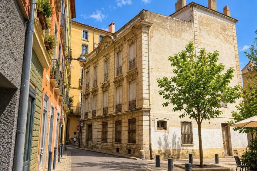 A narrow street with historic buildings, a tree, and bollards. 2