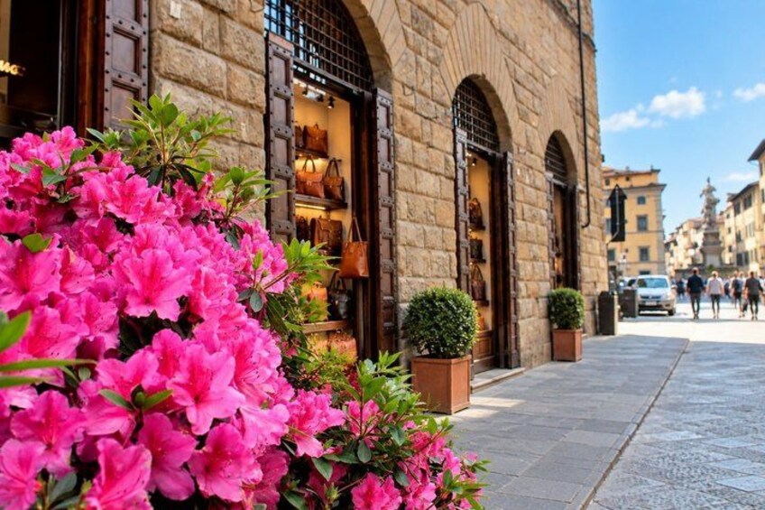 A stone building with arched windows and a sidewalk with pink flowers. 3
