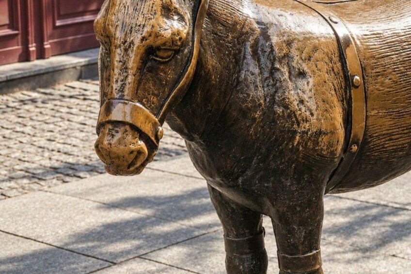A bronze horse statue with a harness on a cobblestone pavement. 5