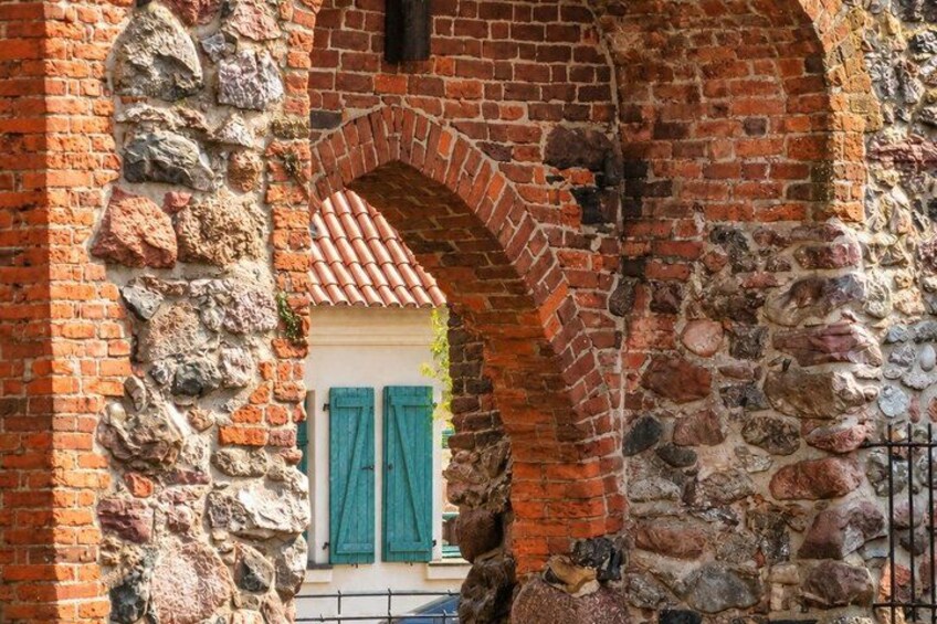 A stone archway with a brick structure, a small building with a tiled roof, and a metal gate. 2