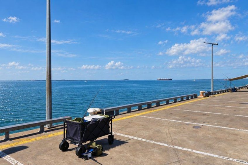 A concrete dock with a fishing cart, a railing, and a ship in the distance. 2