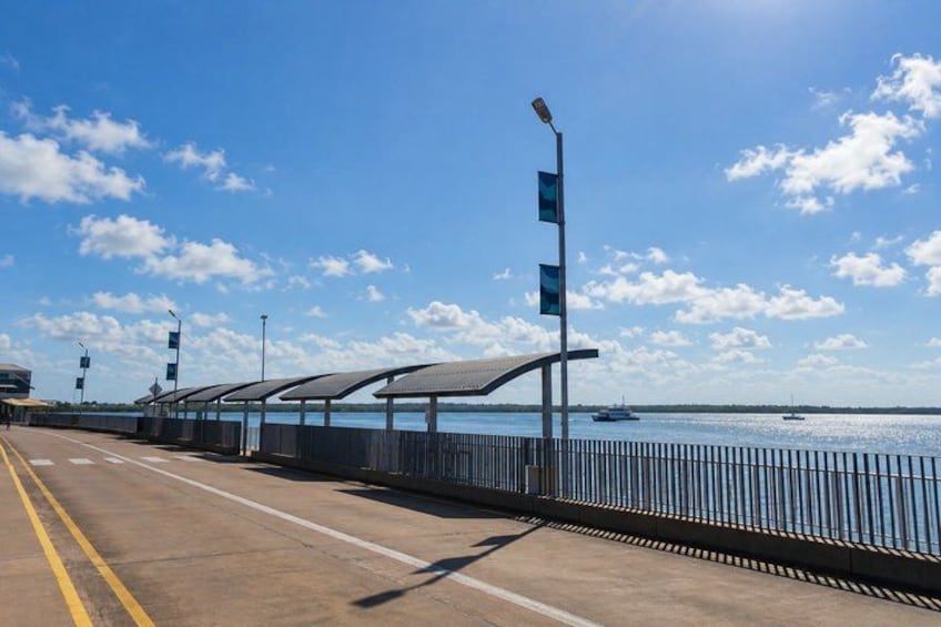A coastal walkway with a metal railing, a clear sky, and boats in the water. 5