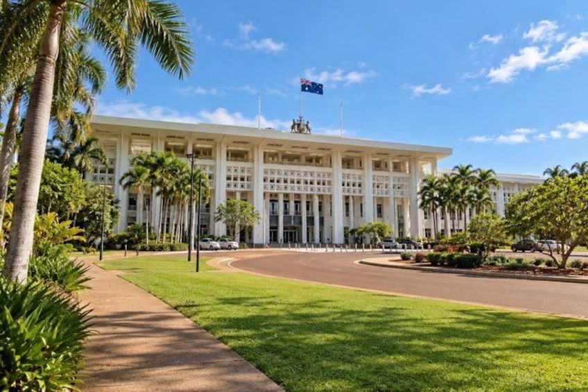 A large white building with a flag, palm trees, and a clear blue sky. 4