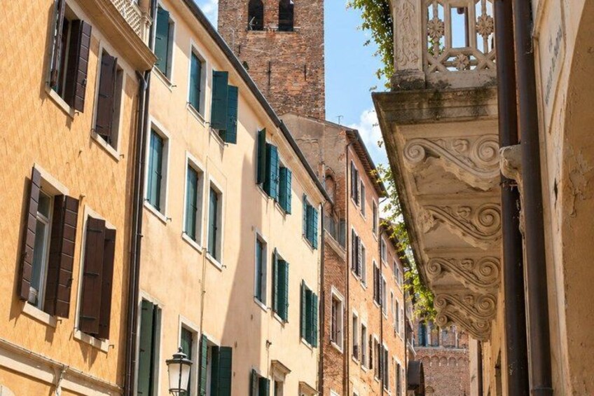 A narrow street with buildings, a tower, and ornate architectural details. 2