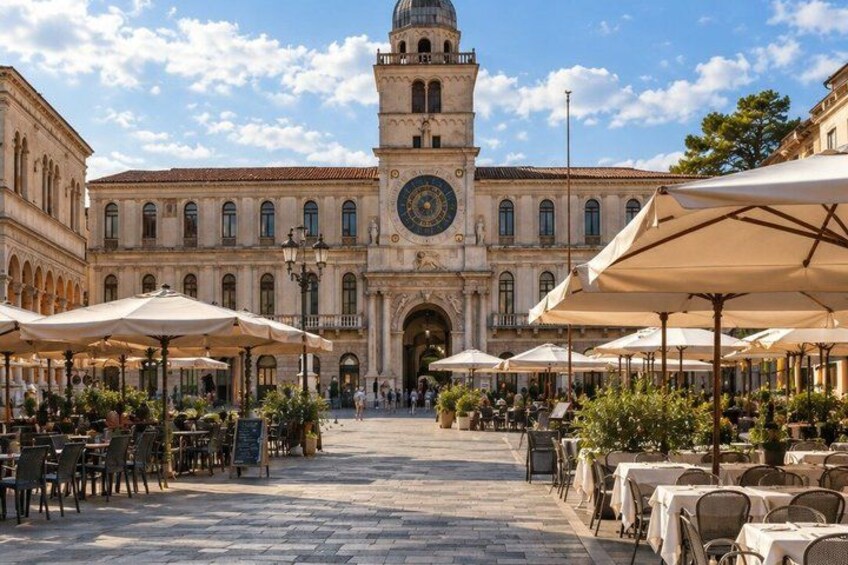 A historic building with a clock tower, outdoor seating with umbrellas, and a paved plaza. 5