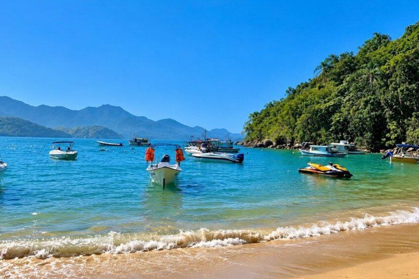 A beach with boats, clear water, and mountains in the background. 4