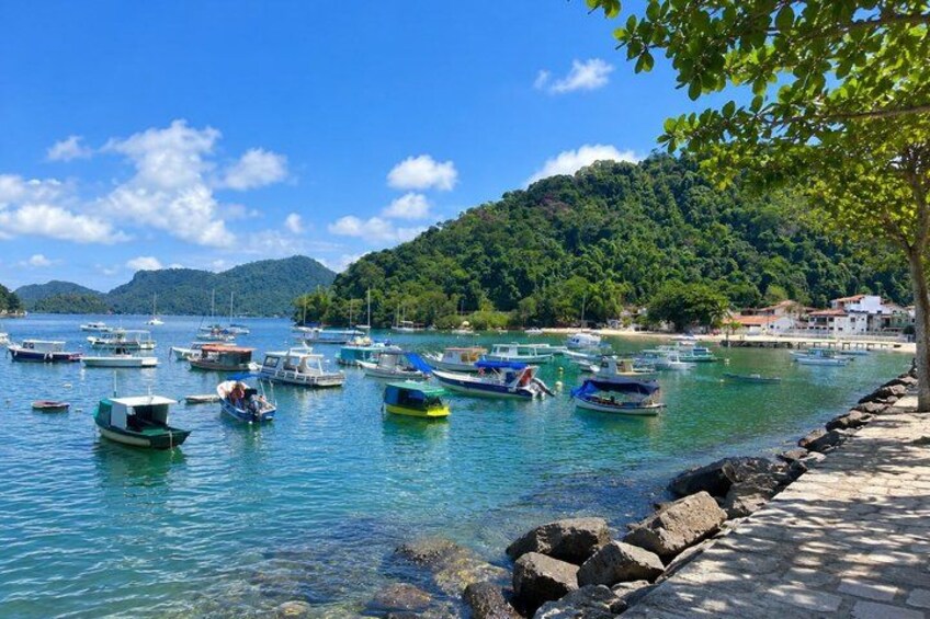 A coastal scene with boats docked along a stone pier, surrounded by lush greenery and hills in the background. 5
