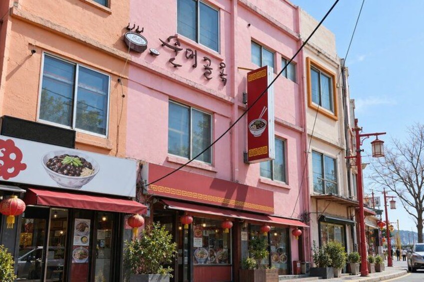 A pink building with a restaurant sign, a red awning, and a red lantern. 4