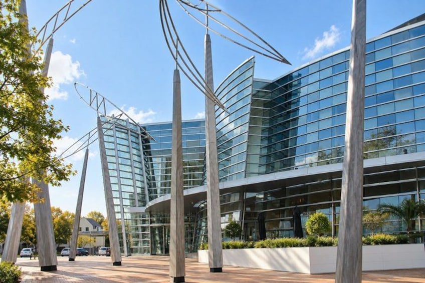A modern building with reflective glass windows, surrounded by a landscaped area with trees and a paved walkway. 1