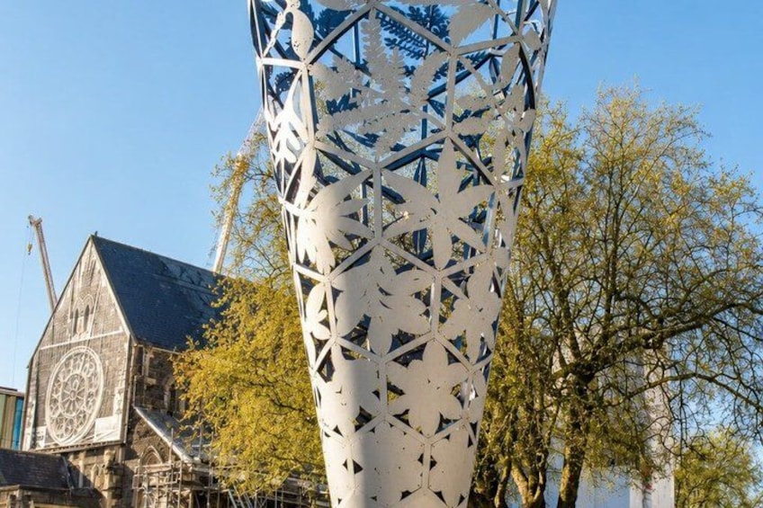 A large metal sculpture with geometric patterns, a church with a clock tower, and autumn trees in the background. 4