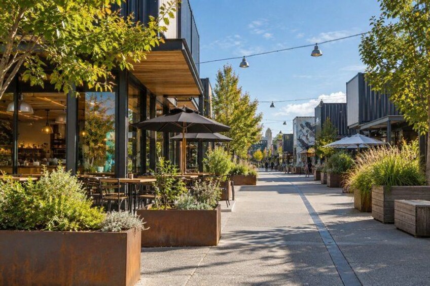 An outdoor cafe area with tables and chairs, surrounded by planters and trees. 5