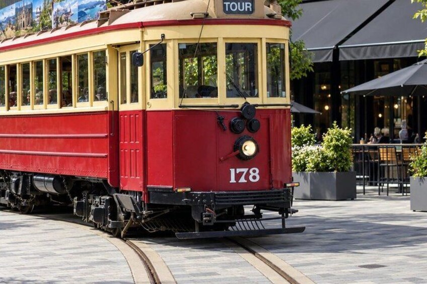 A red and yellow tram numbered 178 on tracks, with a 'TOUR' sign on top, in an outdoor setting with tables and chairs. 2