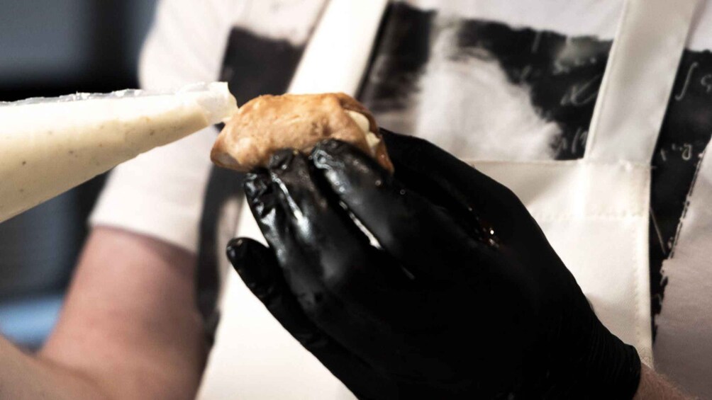 Iemand in zwarte handschoenen behandelt een wit voorwerp, mogelijk eten. 5
